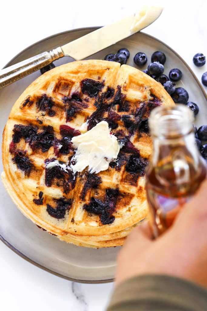 Maple syrup being poured on blueberry waffle.