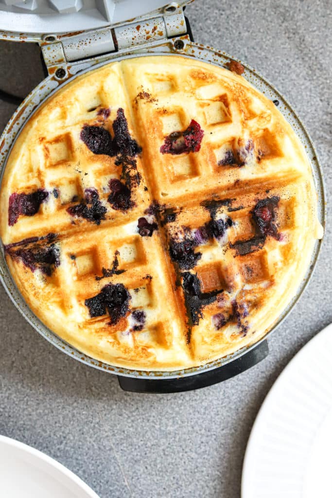 Cooked blueberry waffle in waffle iron.