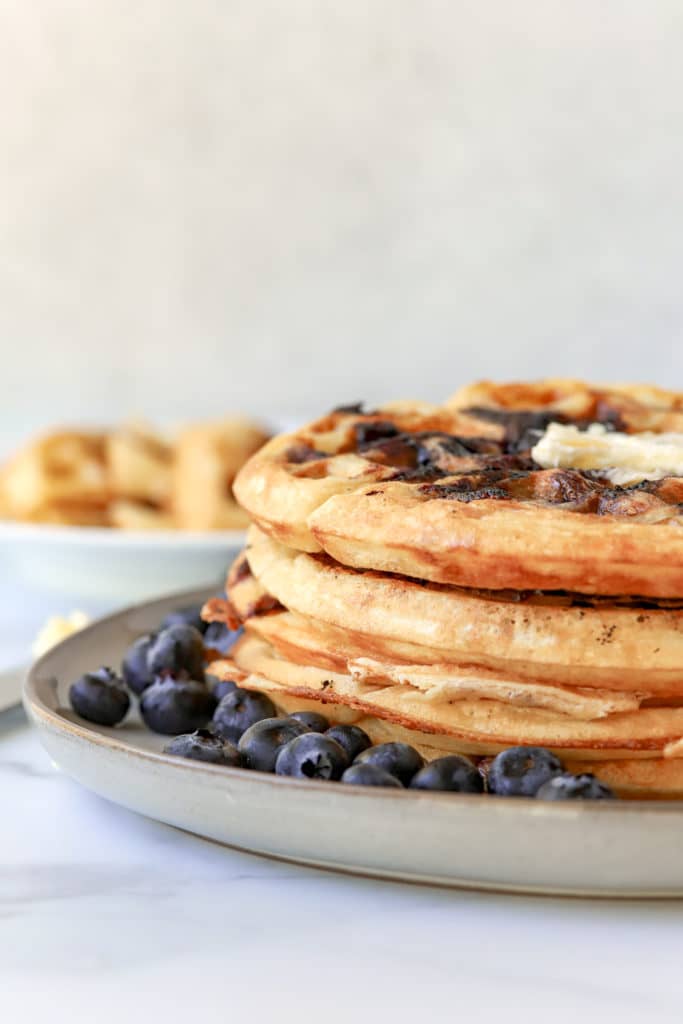 Stacked plate of blueberry waffles topped with fresh blueberries